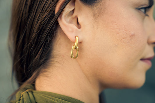 Close-up of a model wearing a gold AWA LINK EARRINGS with a blurred background