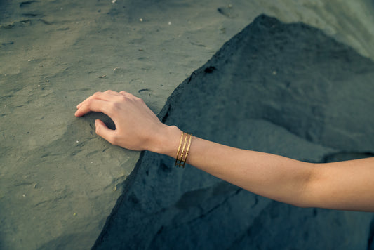 Hand with gold bangle touching a dark stone surface