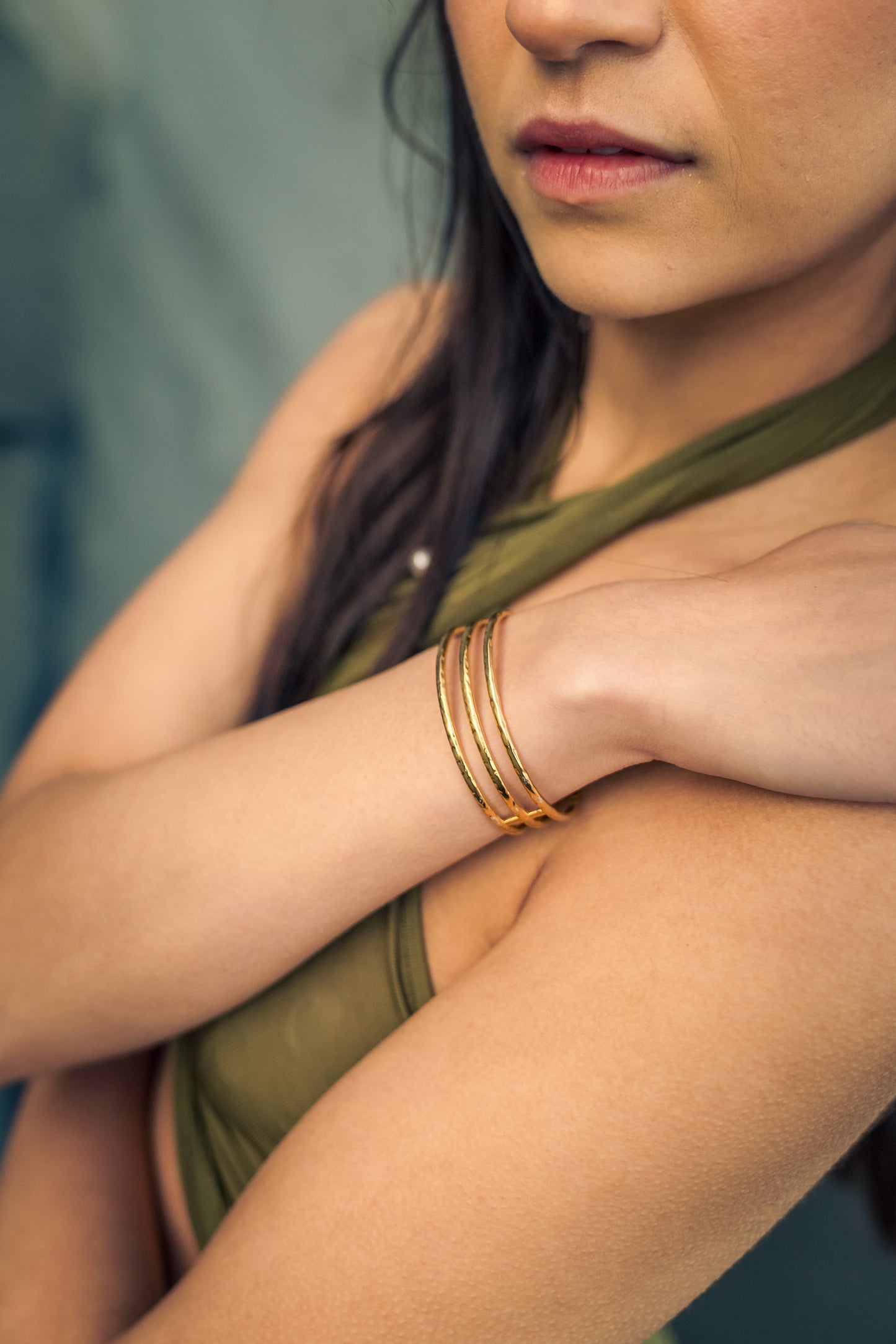Woman wearing a green top and gold bracelets with a blurred background