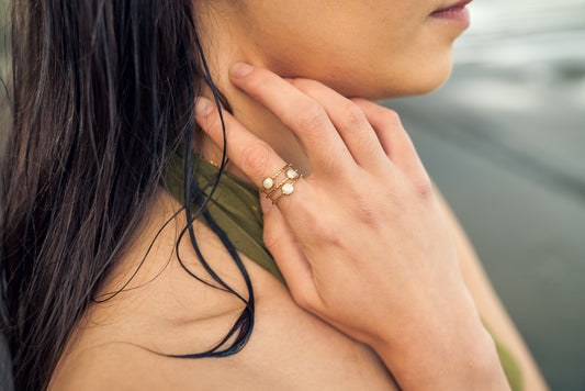 Close-up of a women wearing a gold cuff ring with white stones on their finger, with a blurred background.