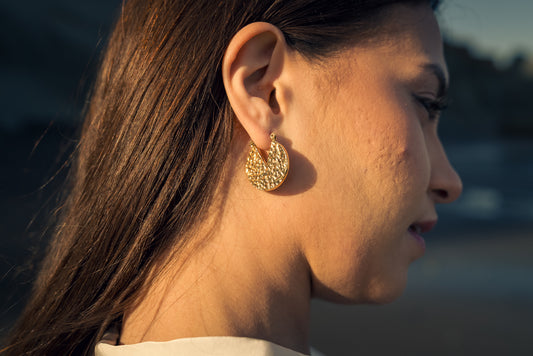 Close-up of a woman wearing gold Dune Hoops earrings with a blurred background