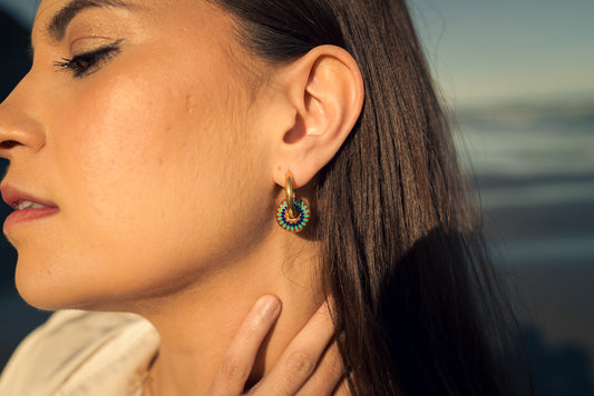 Close-up of a woman wearing colorful Kaleidora hoops earrings with a blurred natural background