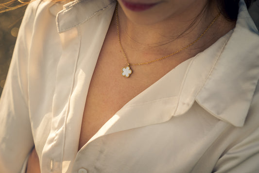Close-up of a women wearing a gold necklace with a clover pendant, against a blurred background.