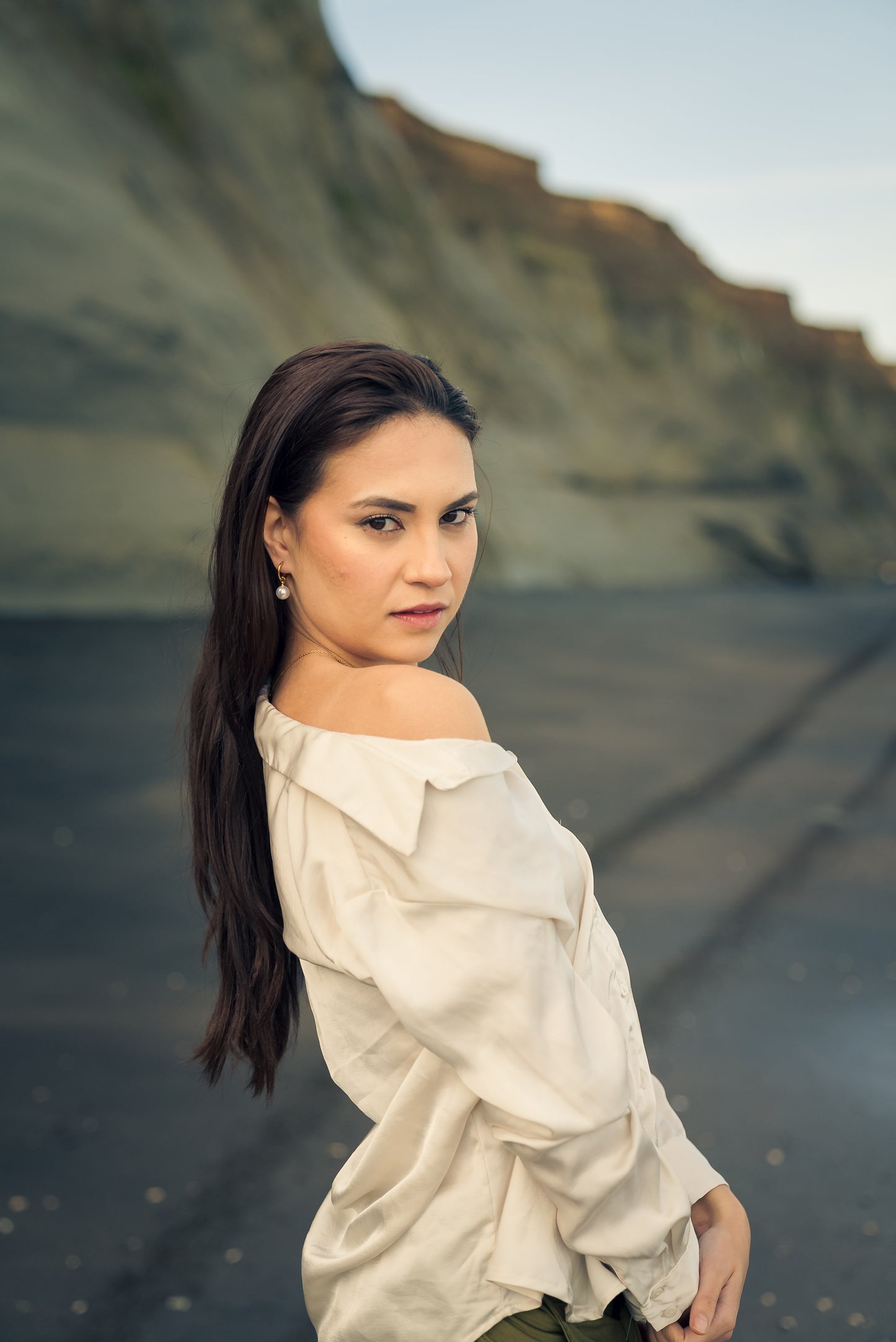 Woman wearing a white off-shoulder top and pearl hoop gold earring standing against a natural background