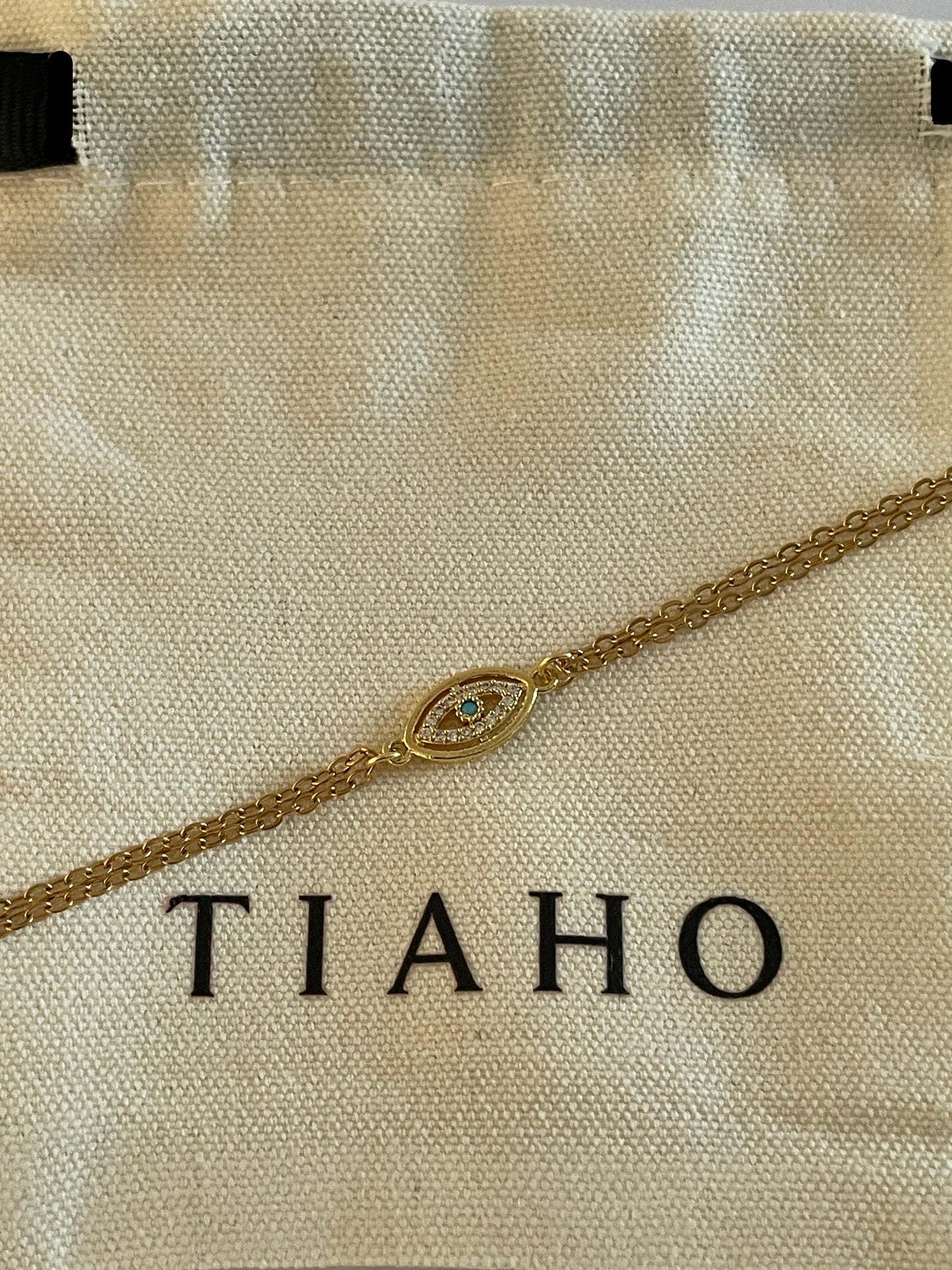Gold evil eye Bracelet on a beige fabric with 'TIAHO' branding