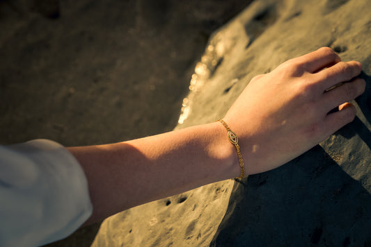 Hand with a gold evil eye bracelet on a sandy surface