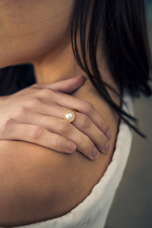 Close-up of a hand wearing a gold ring with a pearl on a blurred background