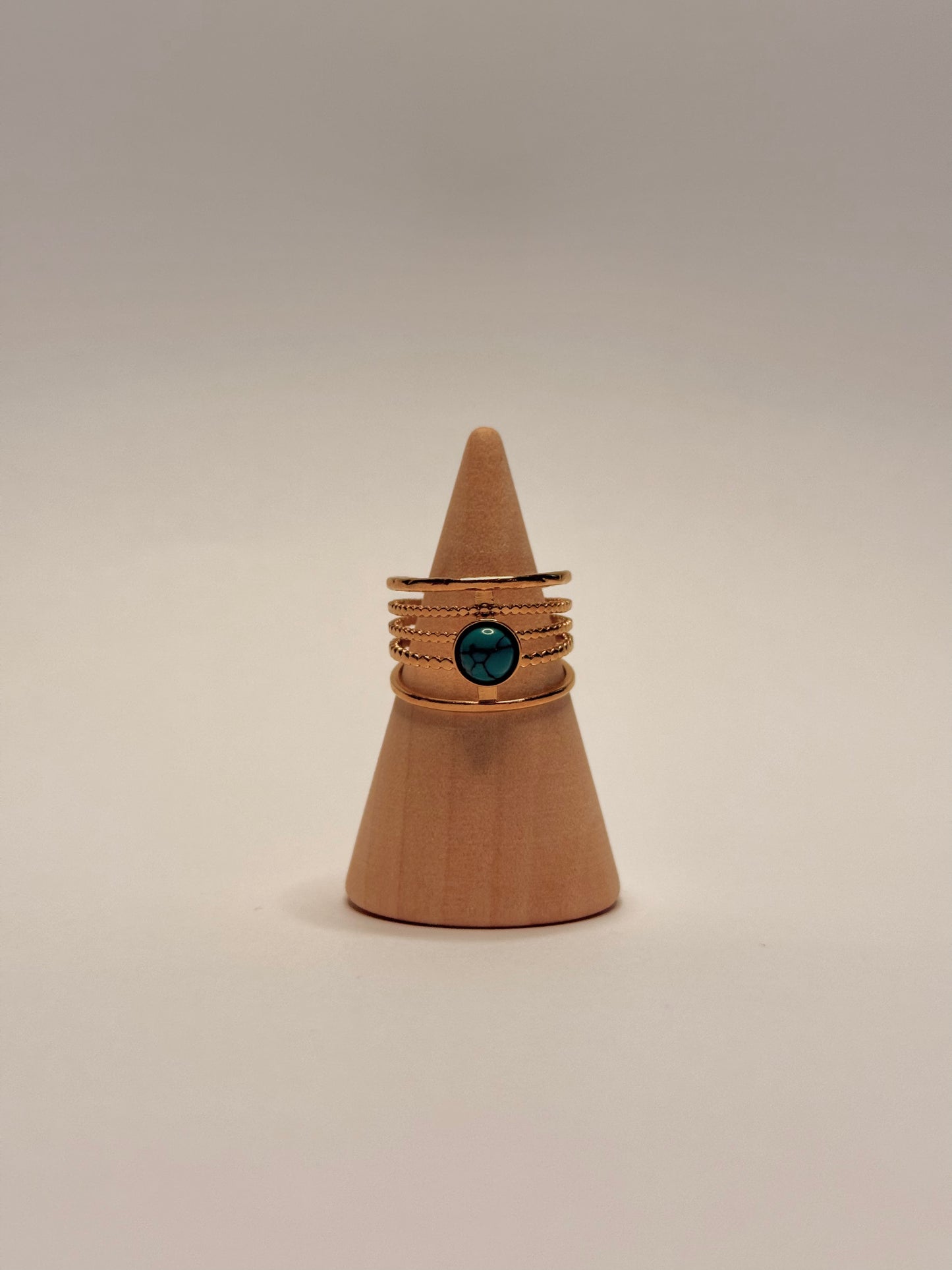 Ring with a turquoise gemstone on a brown cone-shaped stand against a beige background