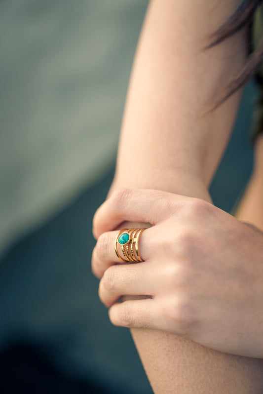Close-up of a hand wearing layered ring with turquoise stone with a blurred background
