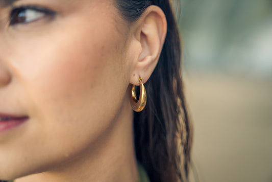 Close-up of a woman wearing gold hoop earrings with a blurred background