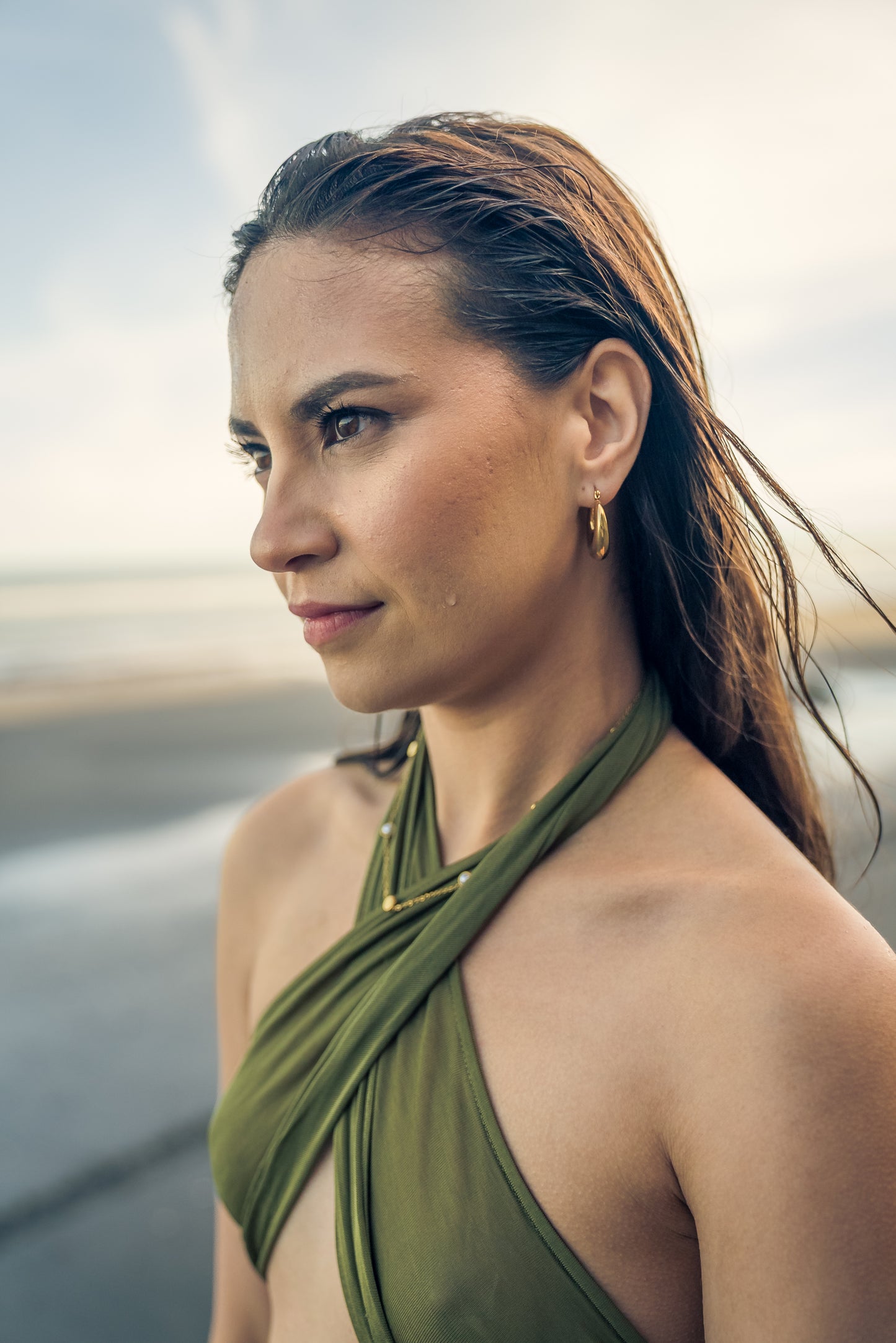 Woman wearing a green halter top and nova hoops with a blurred background
