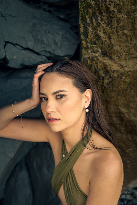Woman in a green dress wearing Pearl bracelets and pearl earring standing against a rocky background