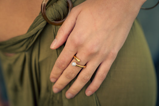 Close-up of a hand wearing a gold ring with a pearl on an olive green garment.