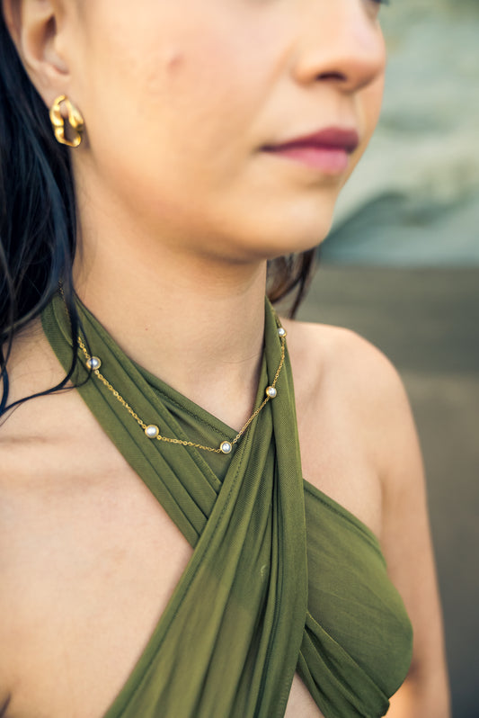 Close-up of a person wearing a green dress with a halter neck design and gold plated jewelry with peals.