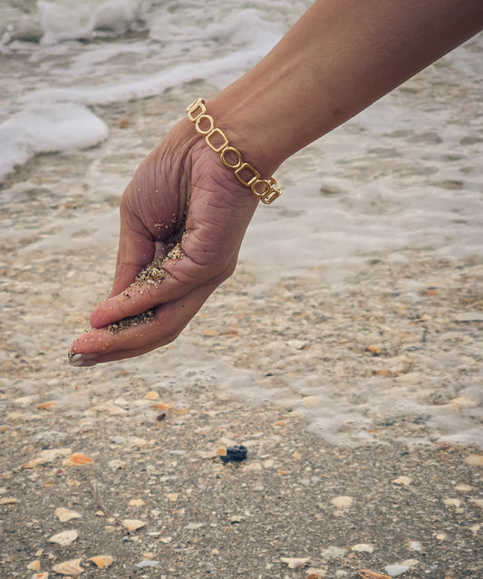 Hand with gold bracelet holding small stones on a beach