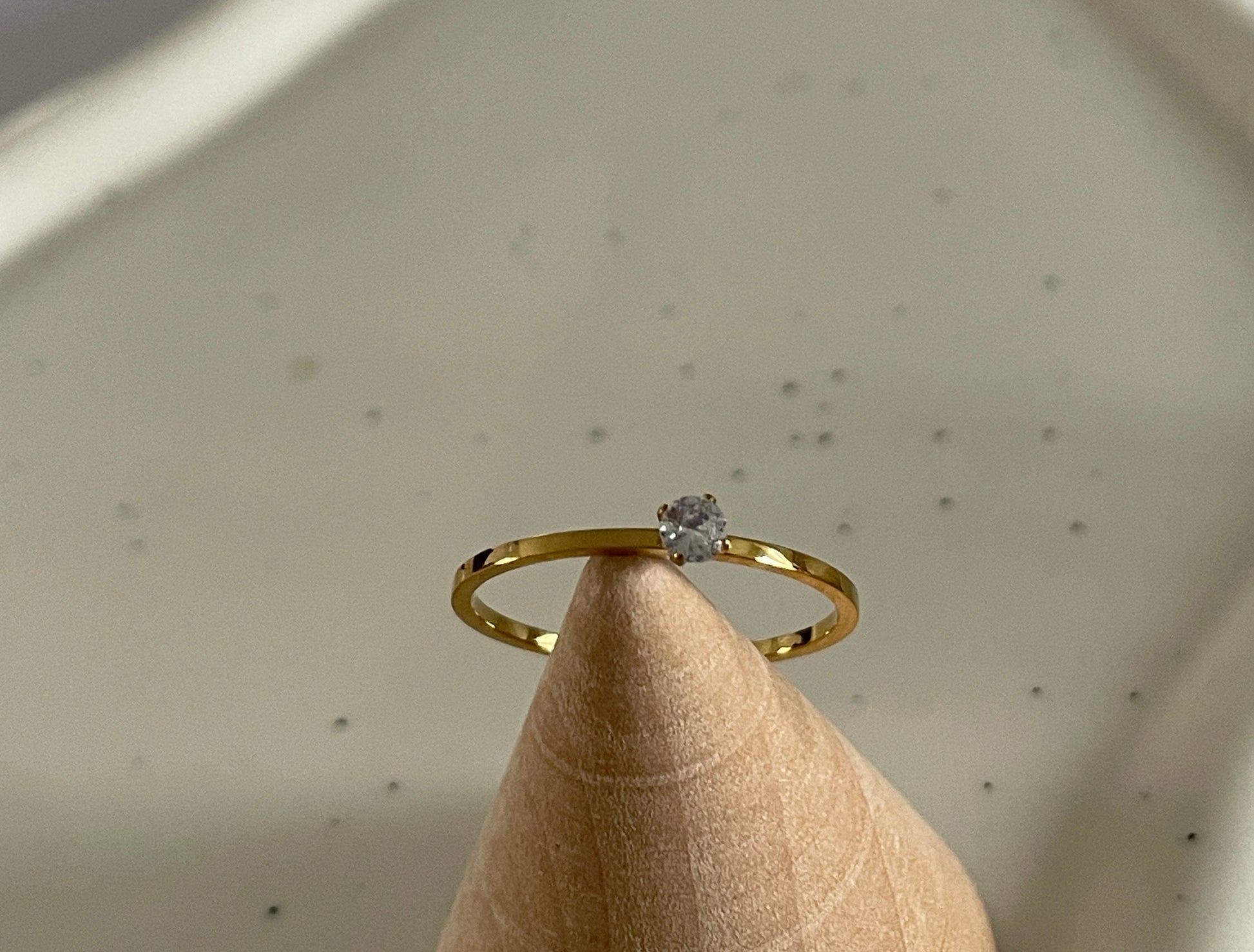Gold ring with a Cubic zirconia stone on a beige stand against a neutral background