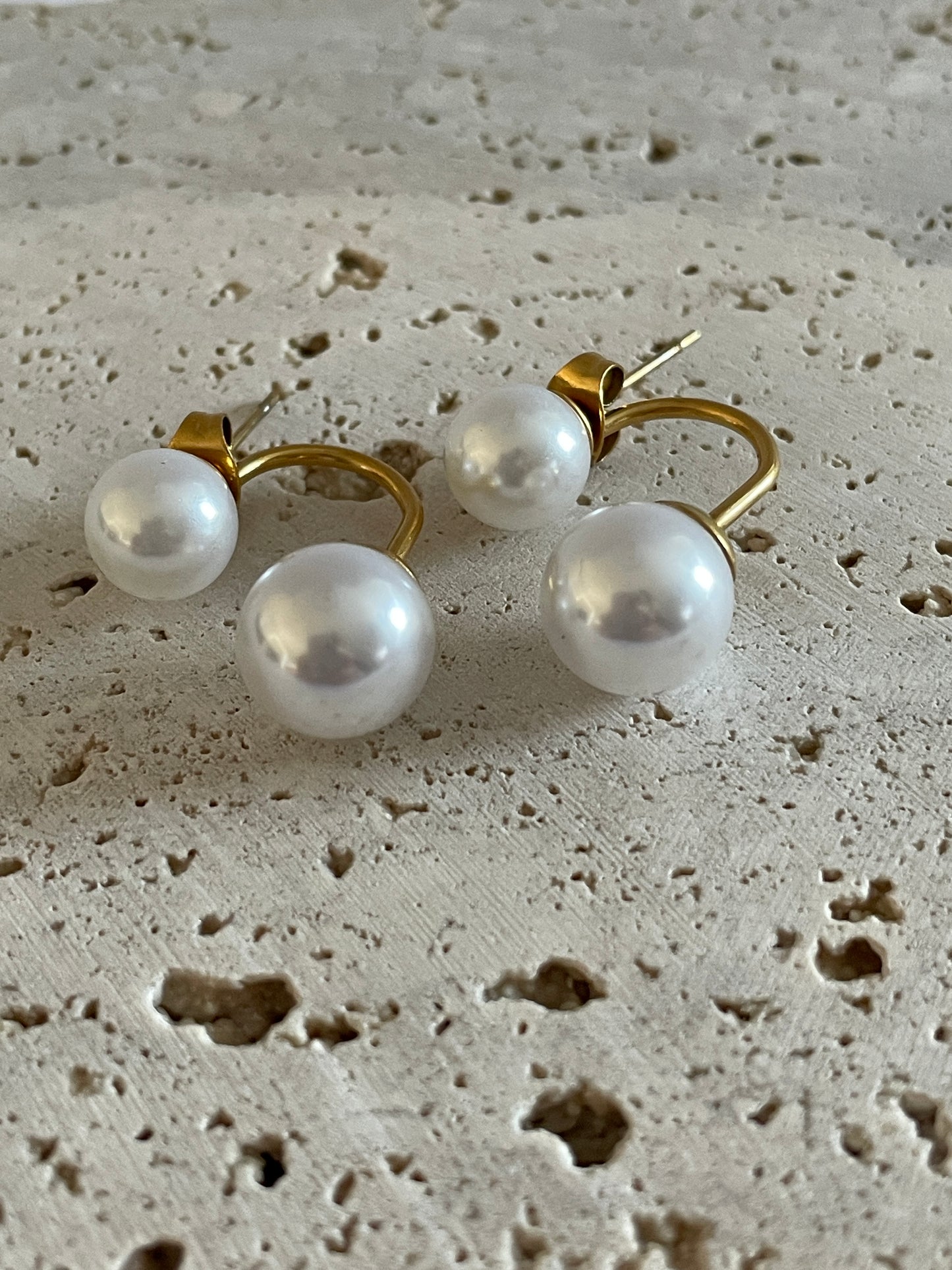 bloom pearl earrings with gold setting on a textured beige surface