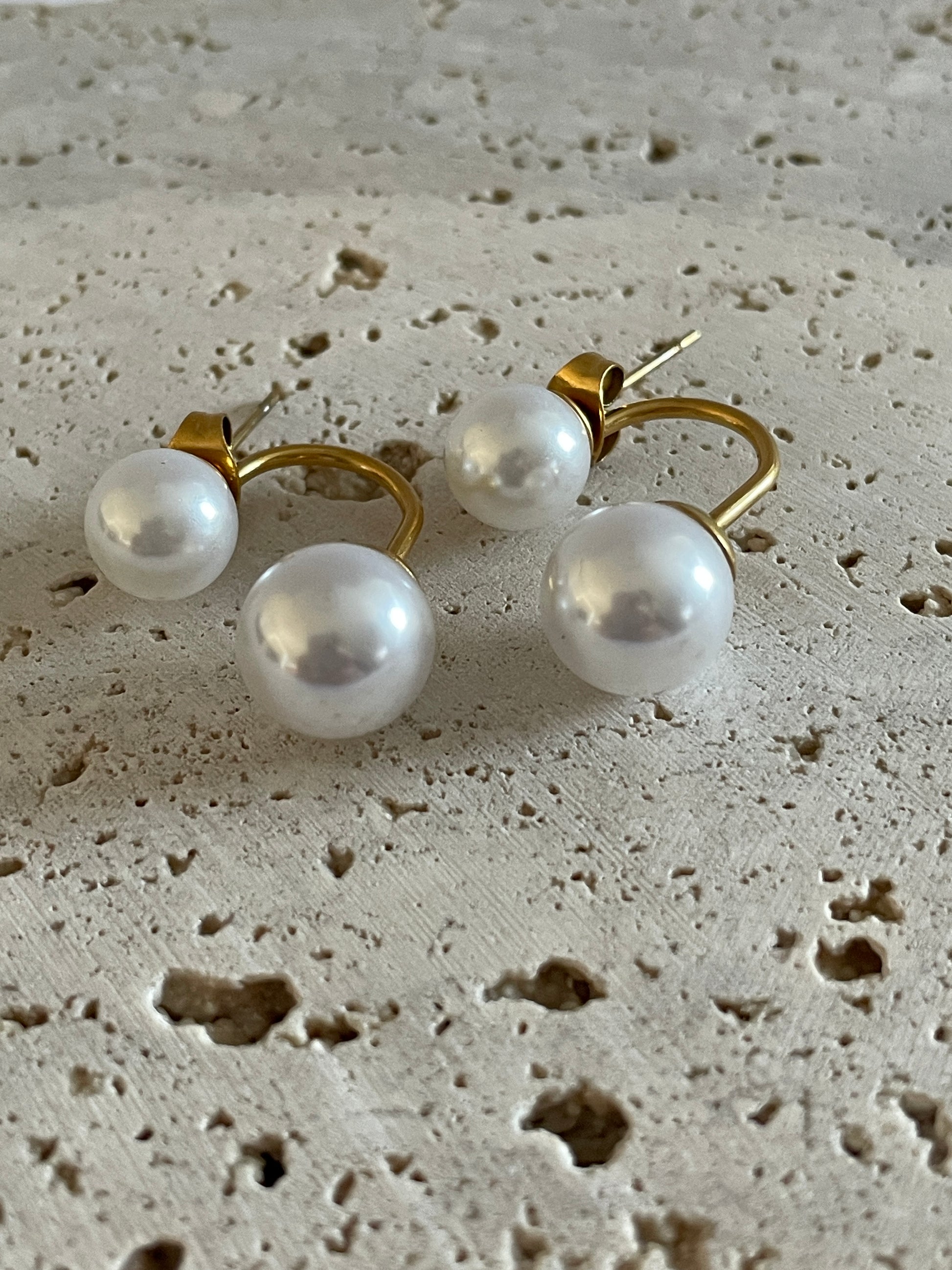 bloom pearl earrings with gold setting on a textured beige surface