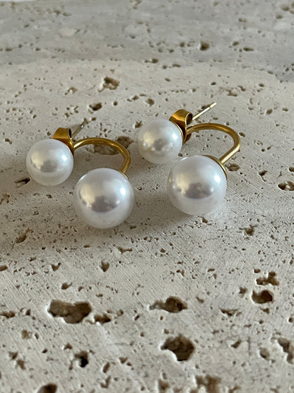 bloom pearl earrings with gold setting on a textured beige surface