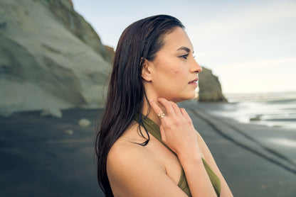 Woman wearing an elegant gold ring  standing on a beach with ocean and cliffs in the background