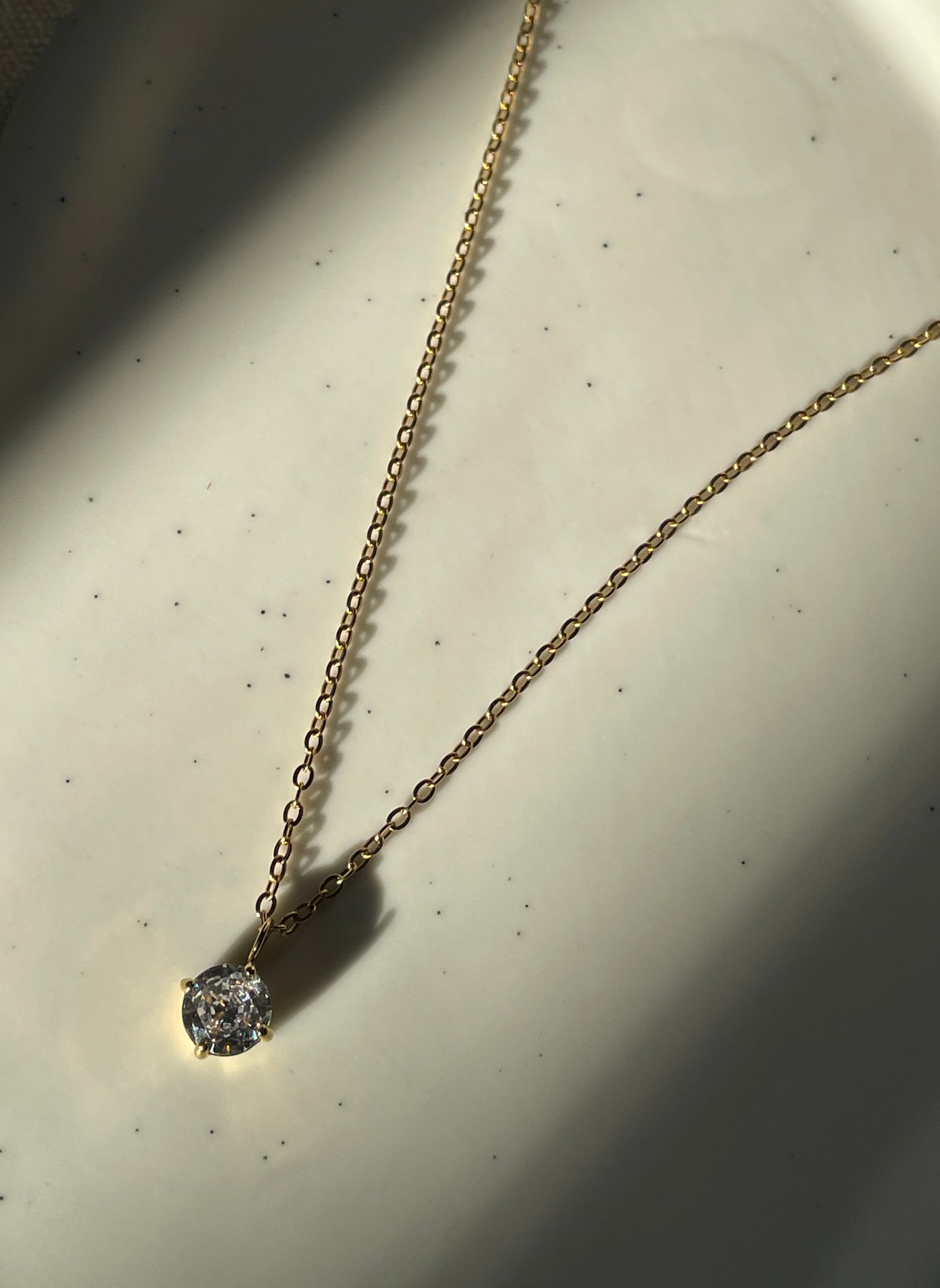 Gold necklace with a cubic zirconia pendant on a light background
