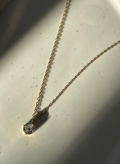 Gold necklace with a cubic zirconia pendant on a light background
