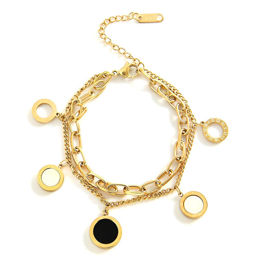 Gold chain bracelet with circular black and white charms on a white background