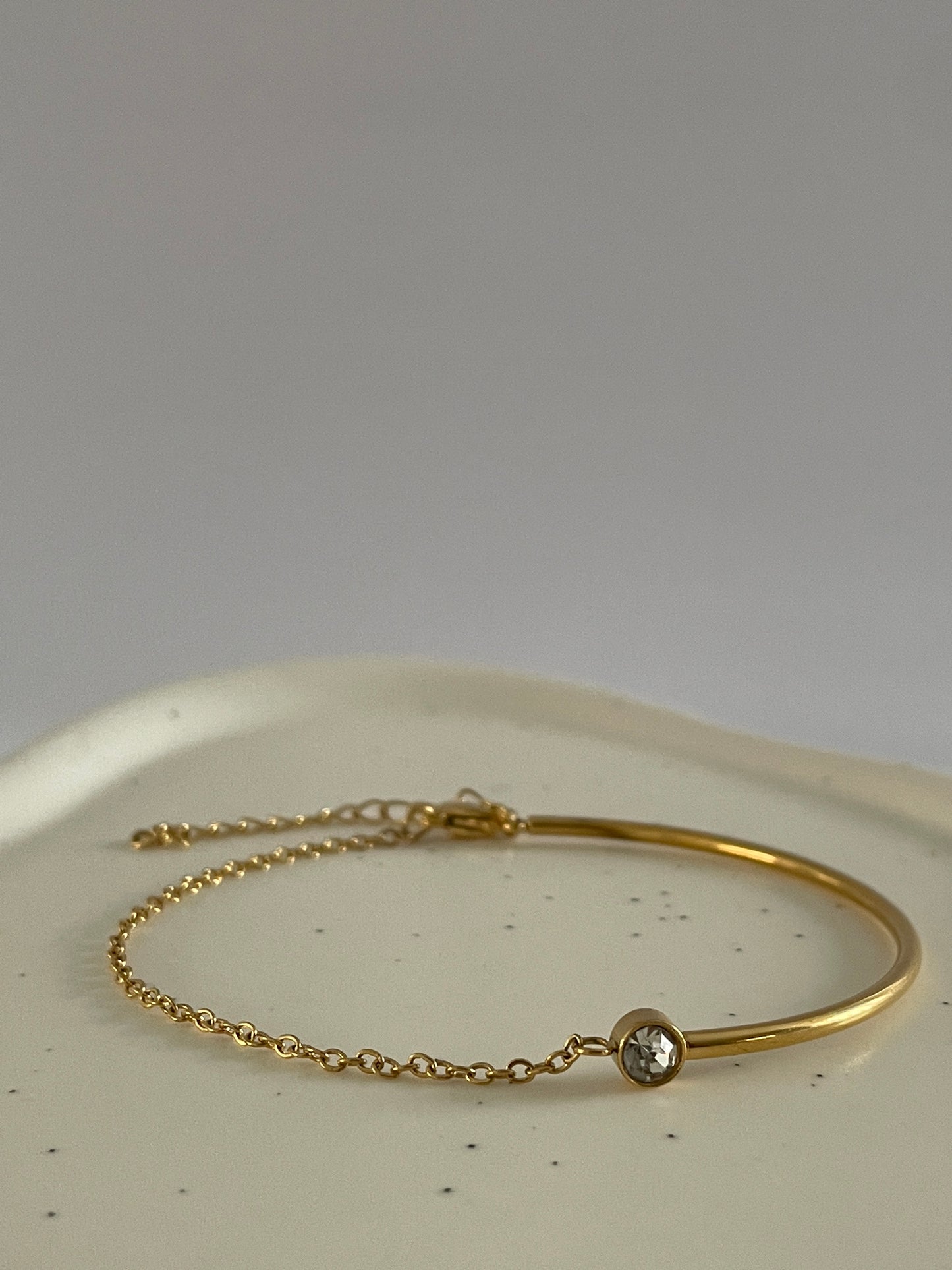 Gold bracelet with a small round cubic zirconia stone on a white surface