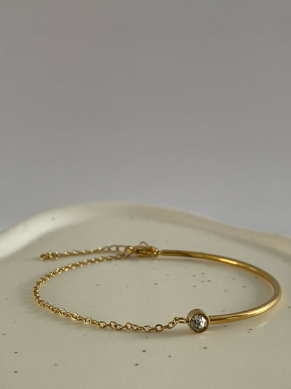 Gold bracelet with a small round cubic zirconia stone on a white surface