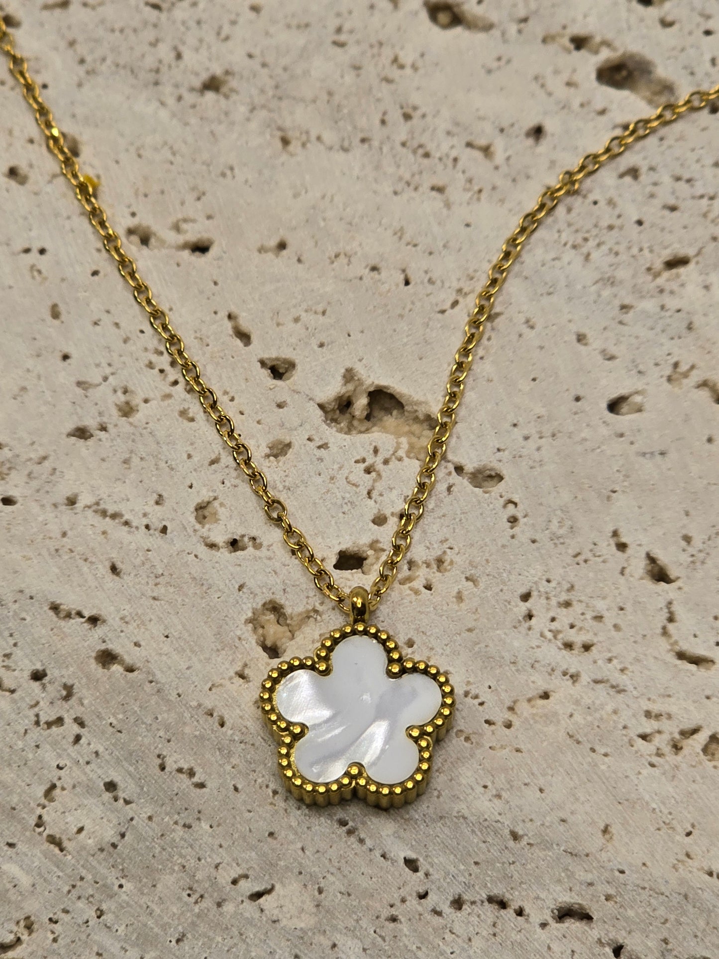 Gold necklace with a clover-shaped pendant on a textured beige surface