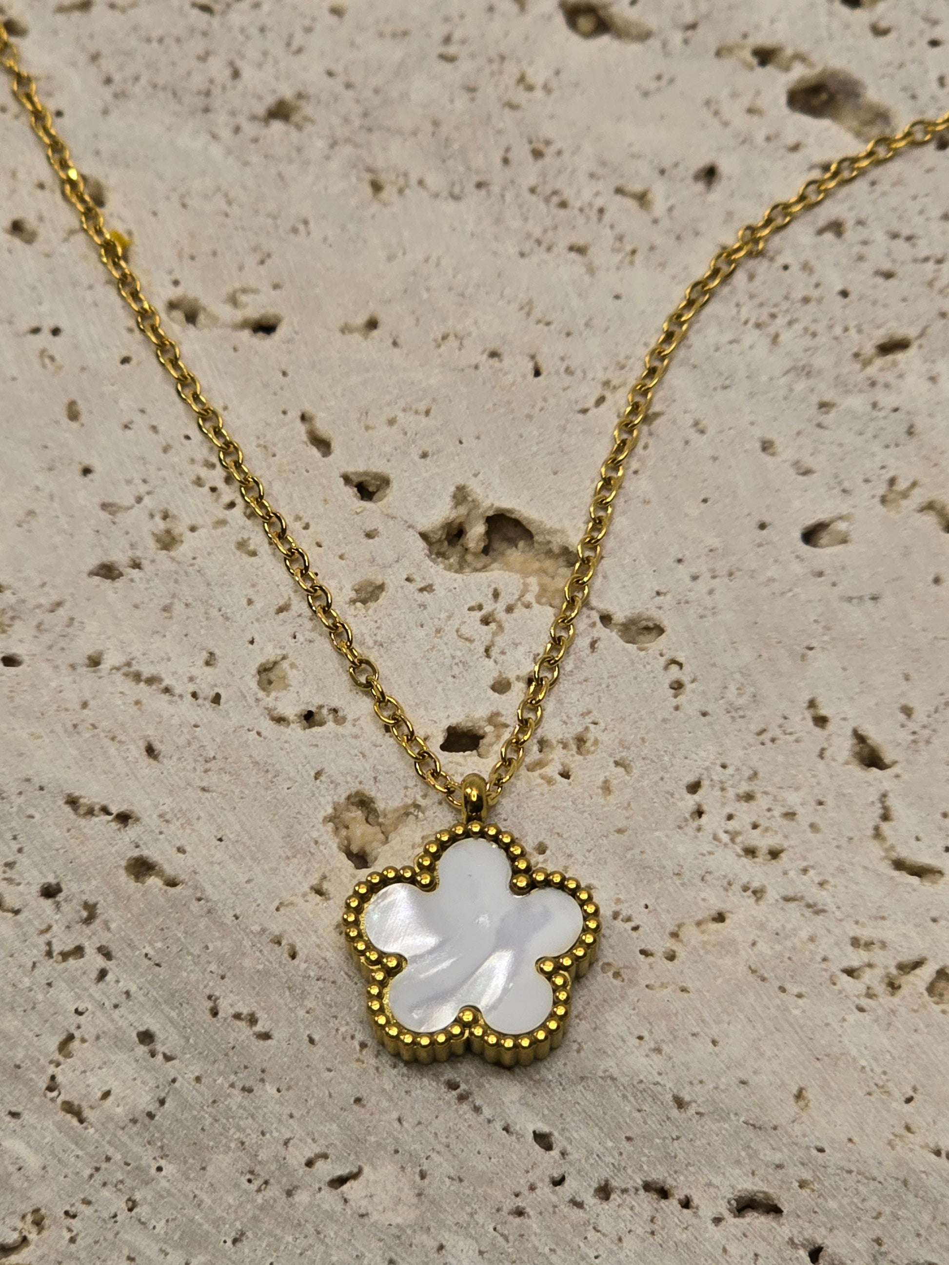 Gold necklace with a clover-shaped pendant on a textured beige surface