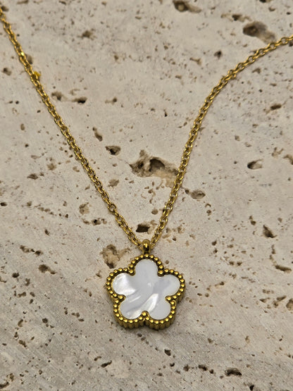 Gold necklace with a clover-shaped pendant on a textured beige surface