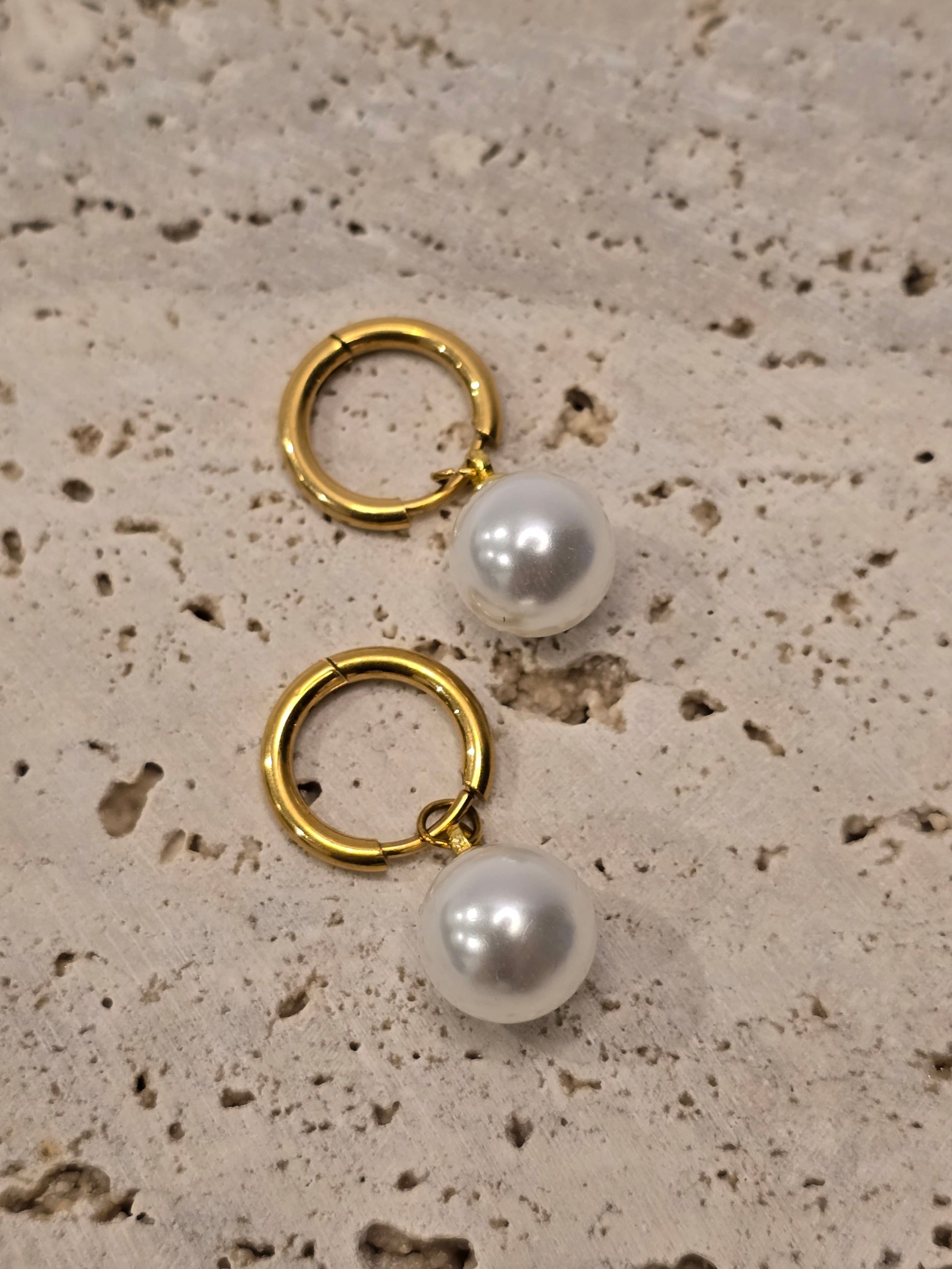 Gold hoop earrings with pearl beads on a textured beige surface