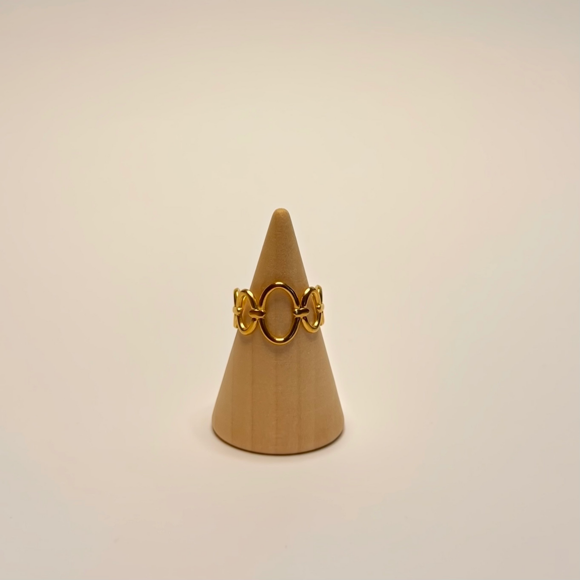 Gold ring on a beige cone-shaped stand against a beige background