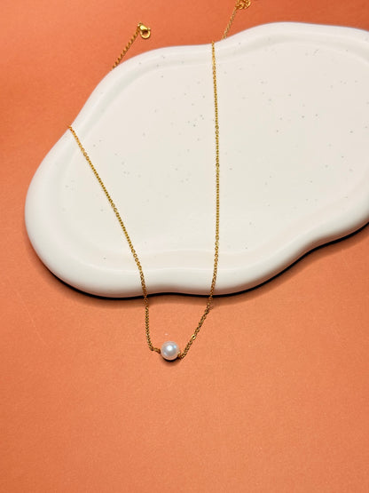 Gold necklace with a pearl pendant on a white stone against an orange background