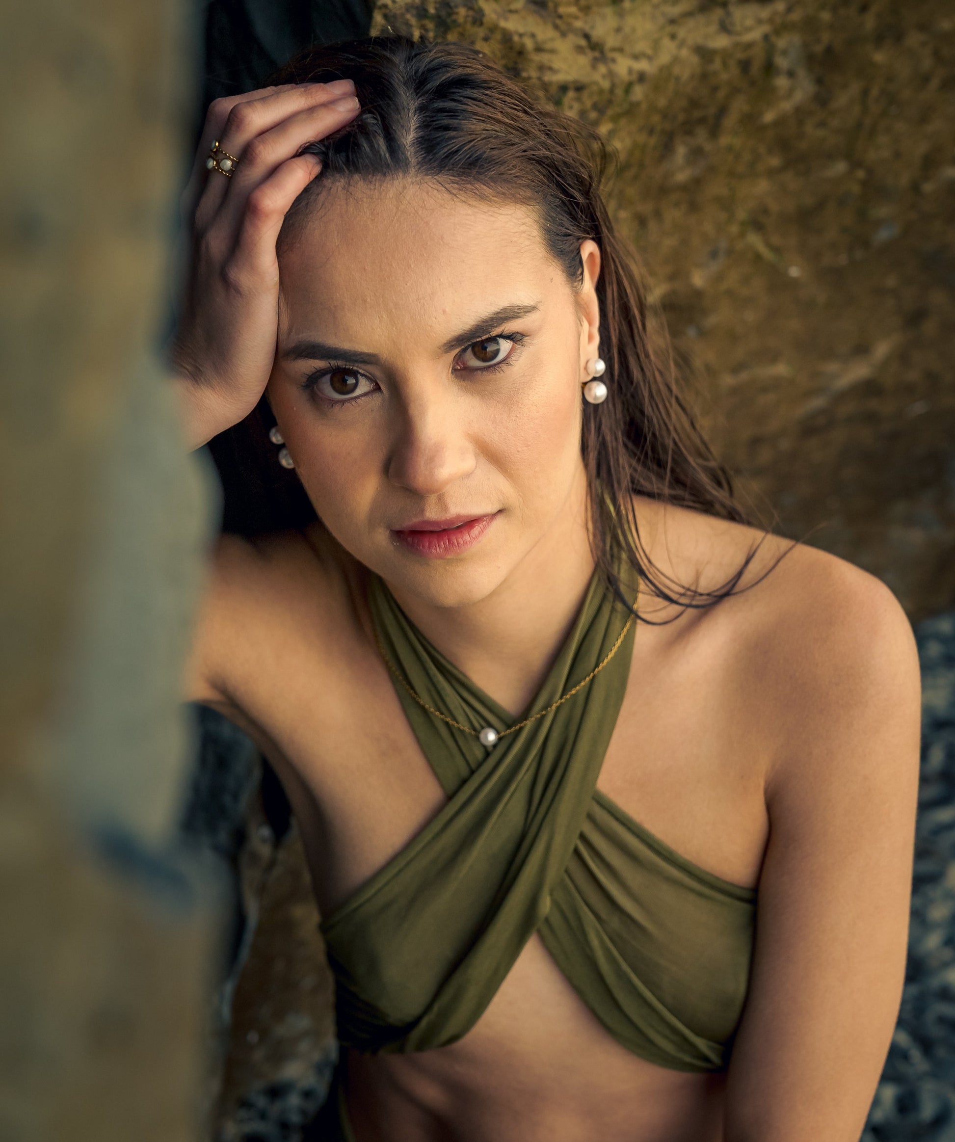 Woman wearing a green top and Noor Pearl Necklace against a textured wall