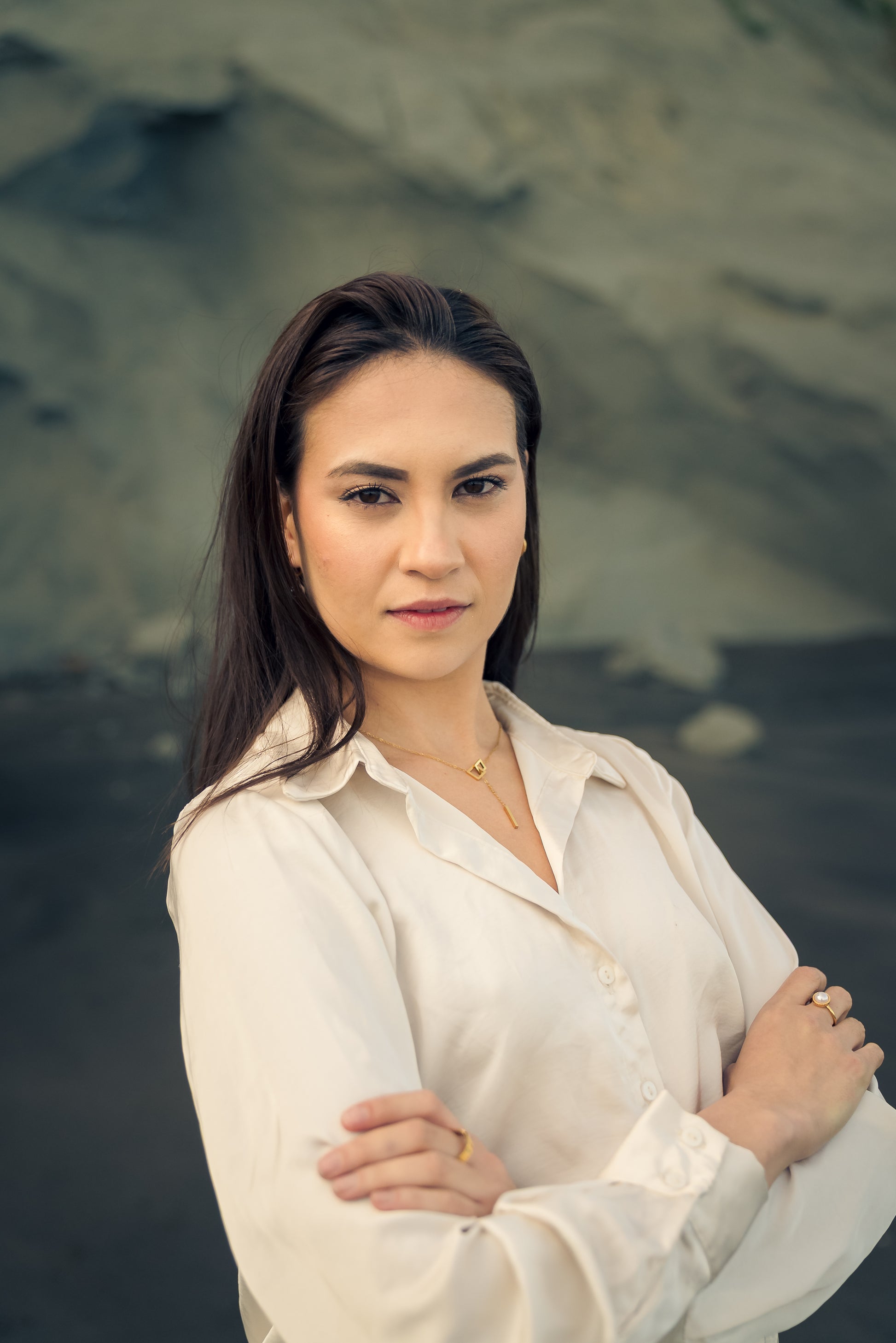 Woman in a white shirt wearing a golden knot pendant necklace standing against a textured wall.