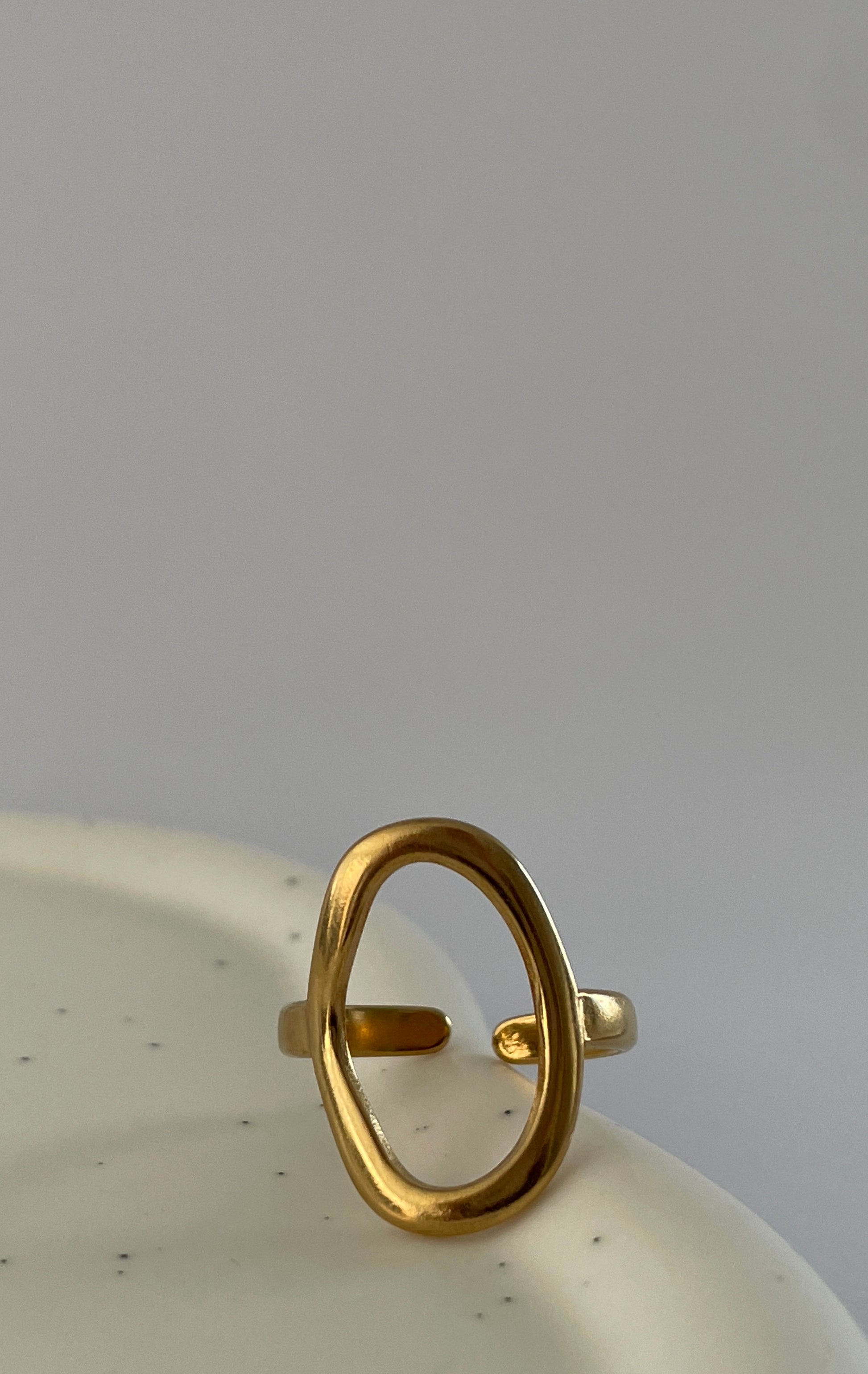 Gold Freeform Open Ring or an Abstract Cuff Ring on a textured white surface with a gray background