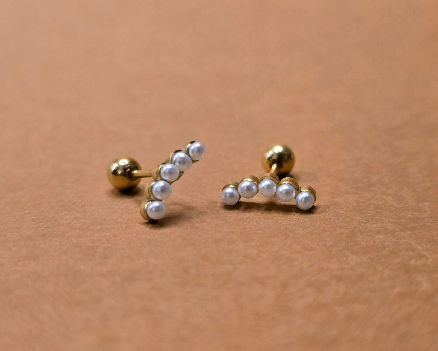 Pair of gold and pearl stud earrings on a beige background
