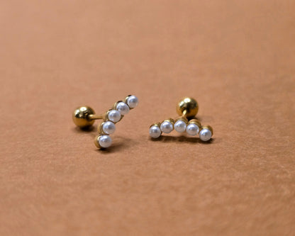 Pair of gold and pearl stud earrings on a beige background