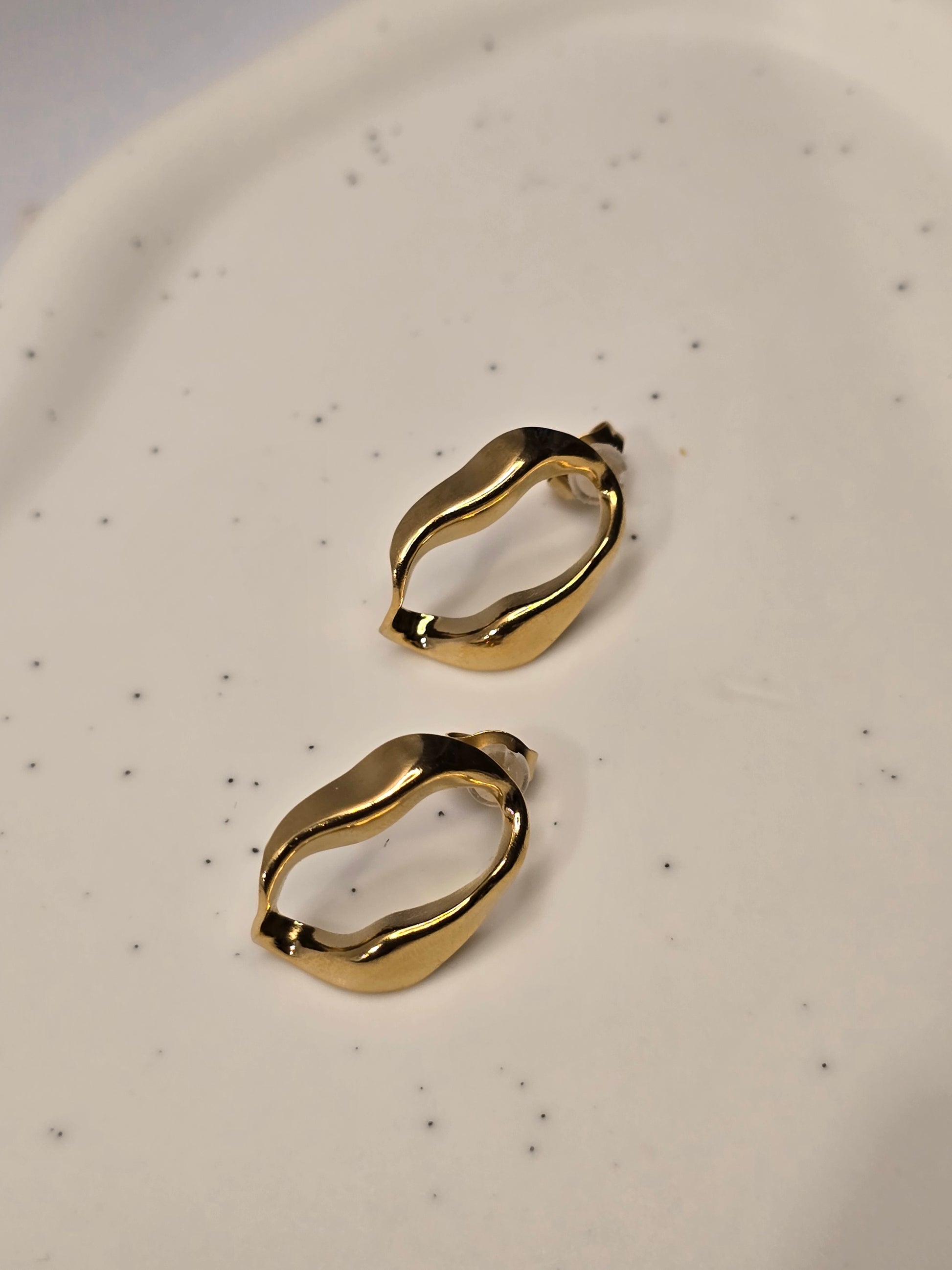 Wave Aura Gold hoop earrings on a speckled beige plate