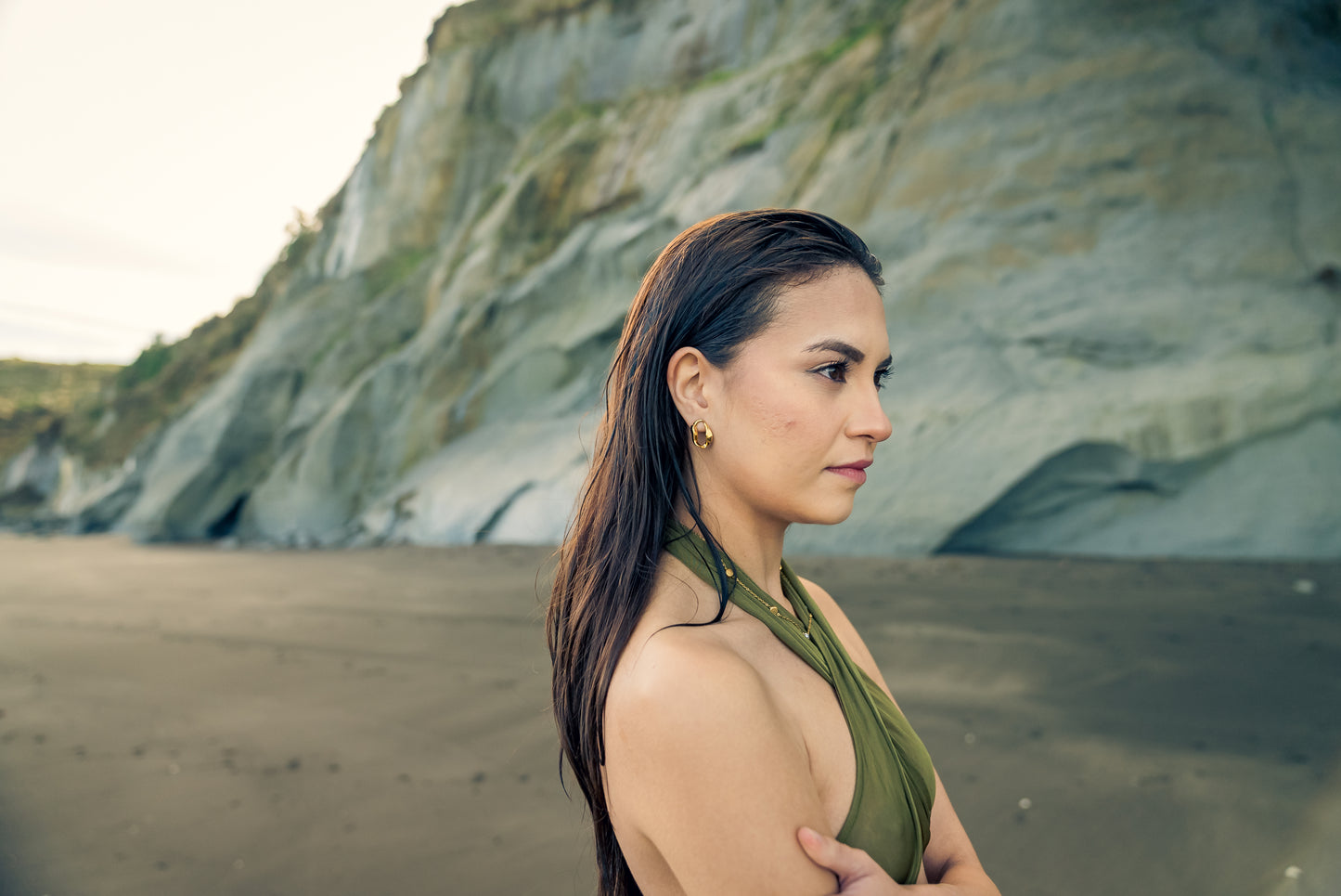 Model standing on a beach with cliffs in the background wearing Wave Aura earrings