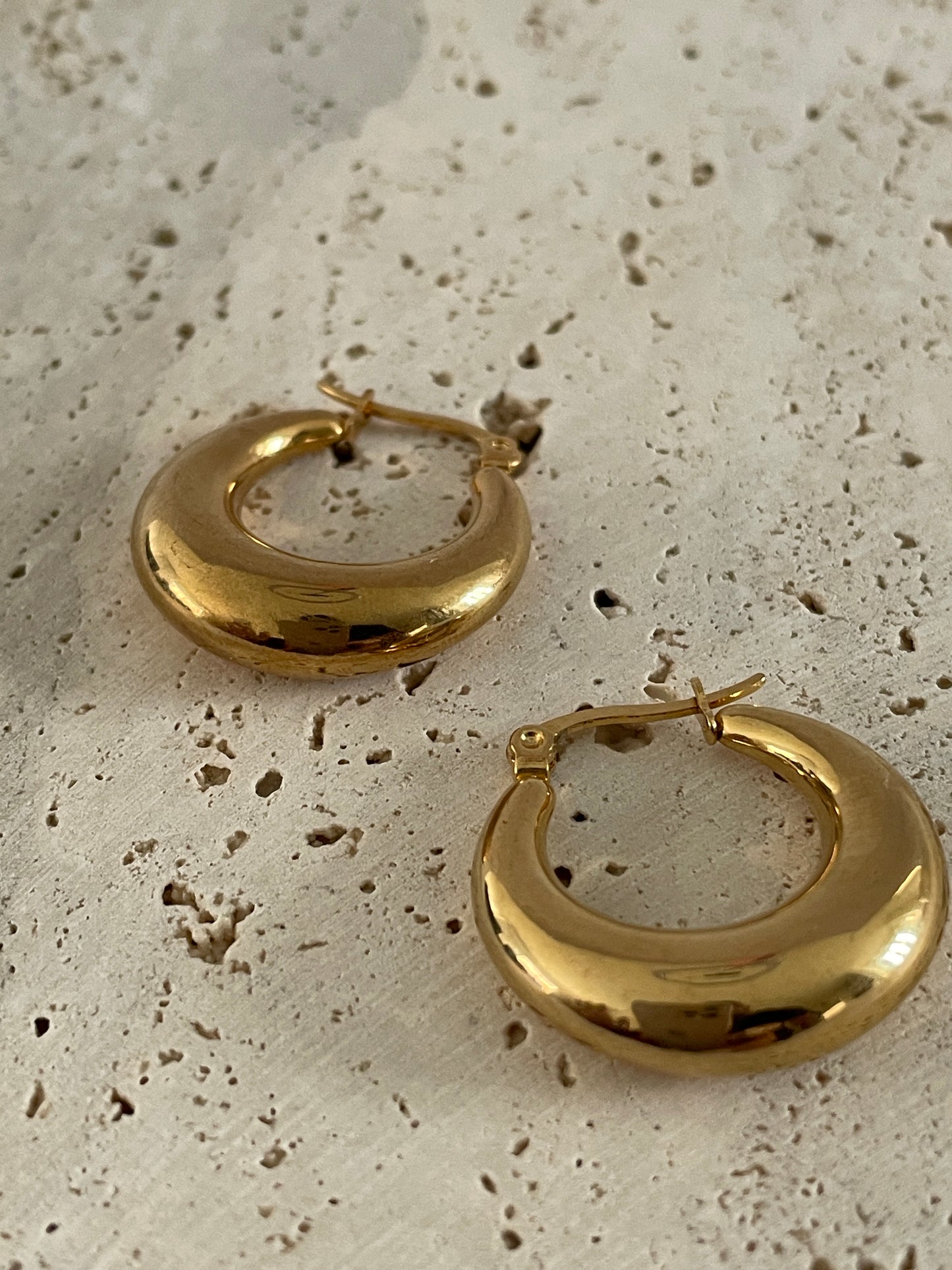 Gold hoop earrings on a textured beige surface
